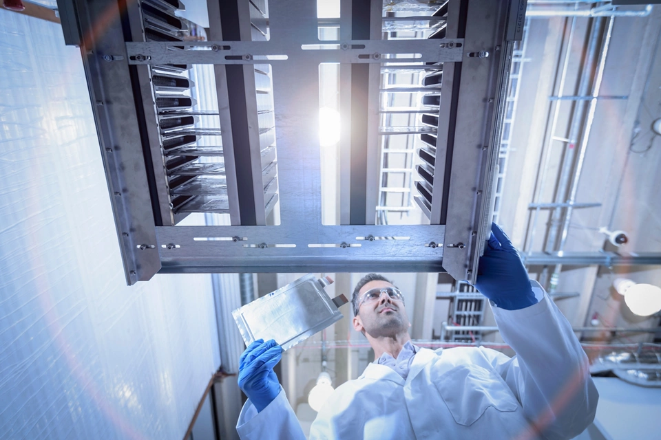 Scientist with lithium ion pouch cell manufacture machine in battery research facility, low angle view