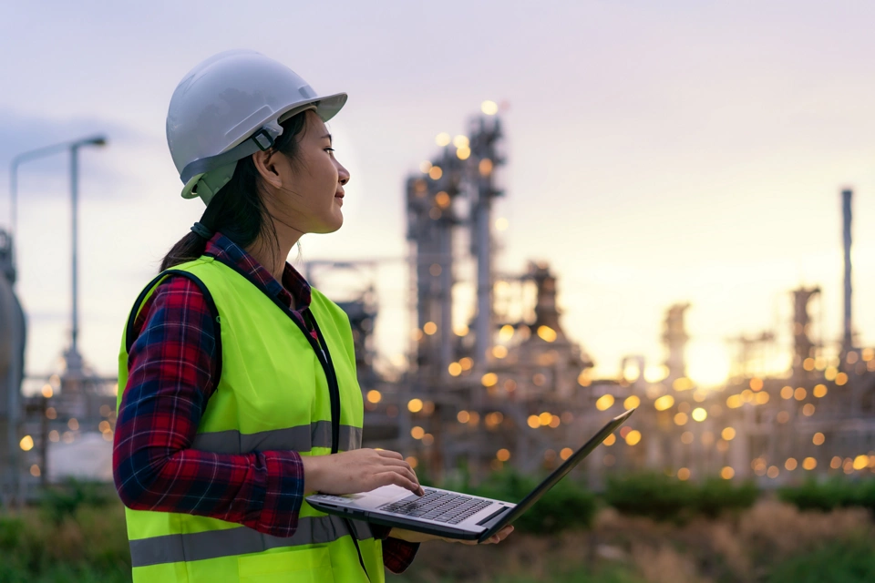 Asian woman petrochemical engineer working at night with laptop Inside oil and gas refinery plant industry factory at night for inspector safety quality control.