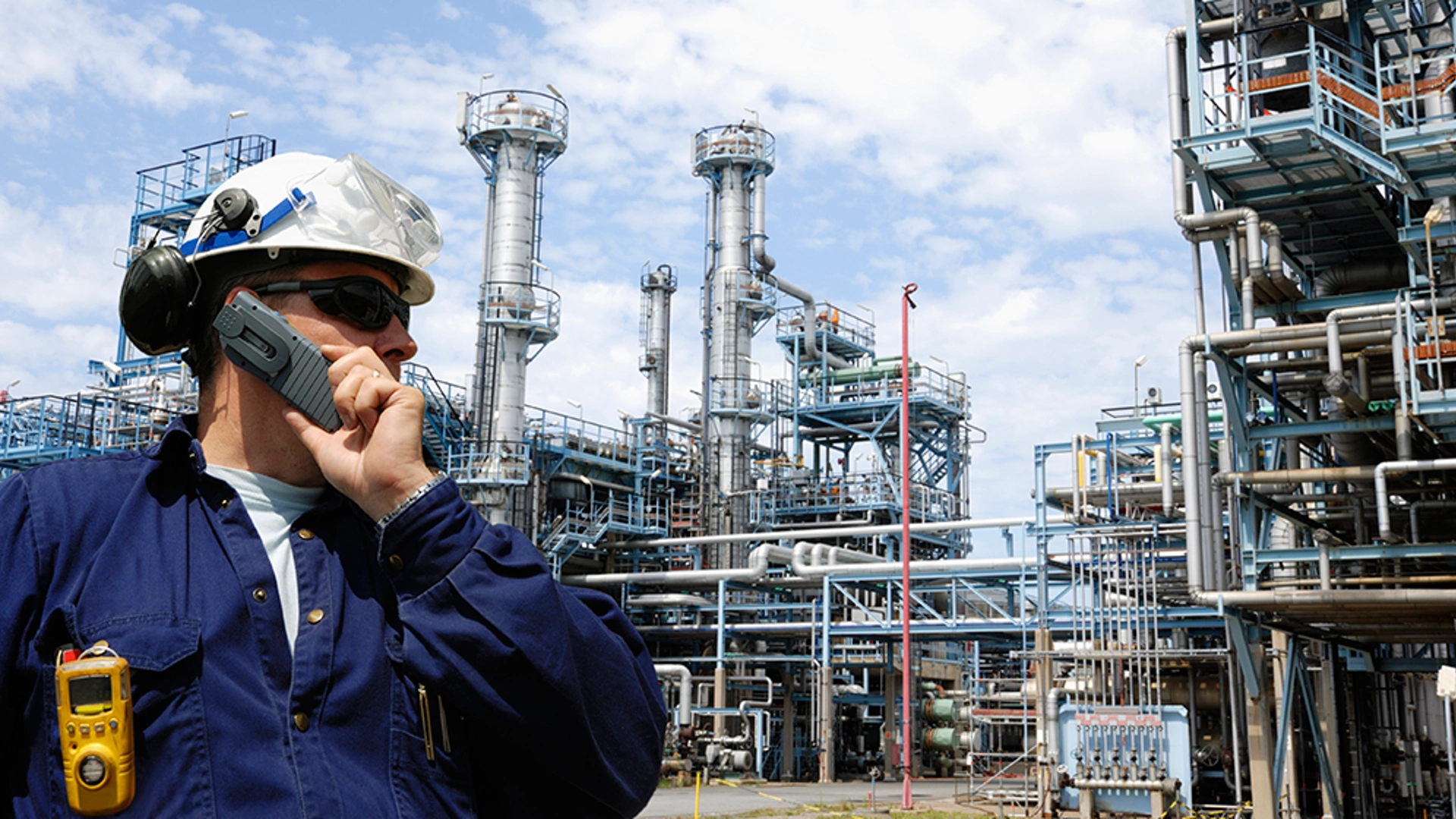 engineer talking in mobile-phone with large oil refinery in background ( slightly out of focus )