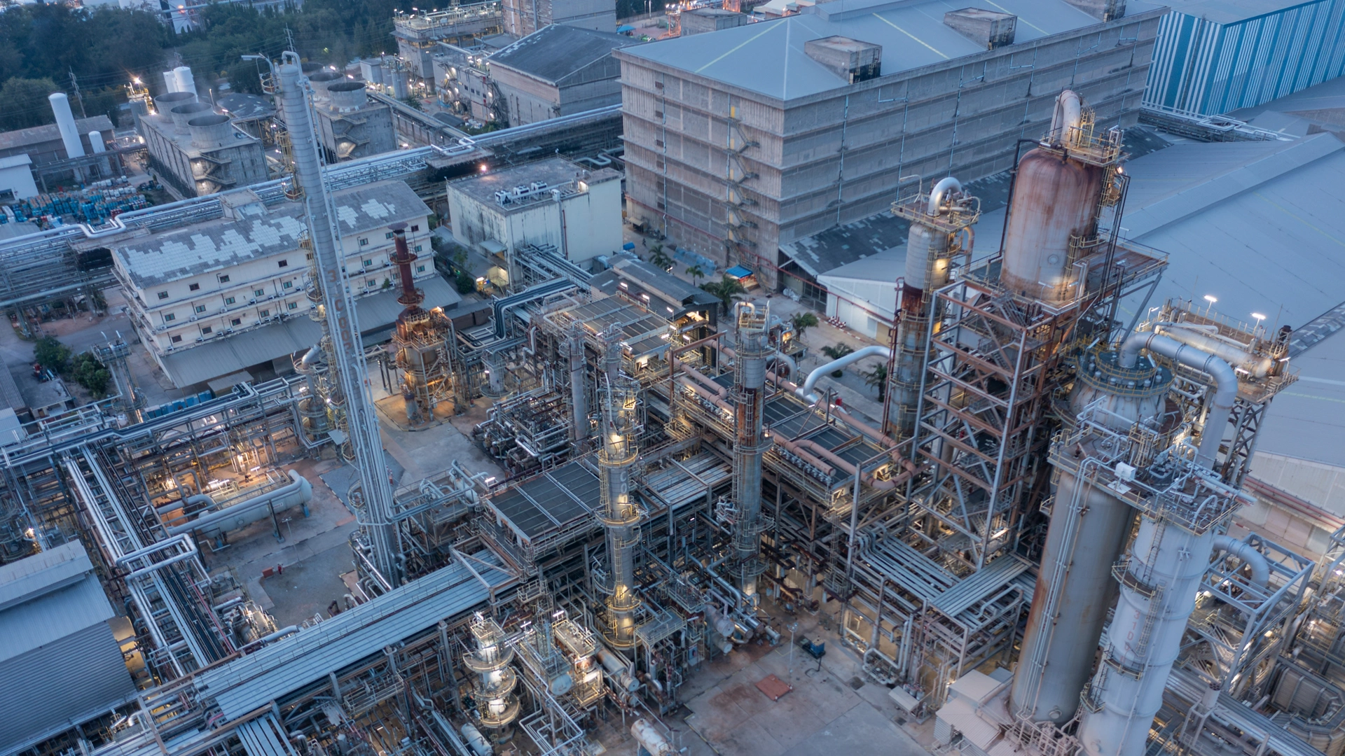 Twilight descends on a sprawling chemical facility, its network of pipes and reactors illuminated, signifying relentless production.