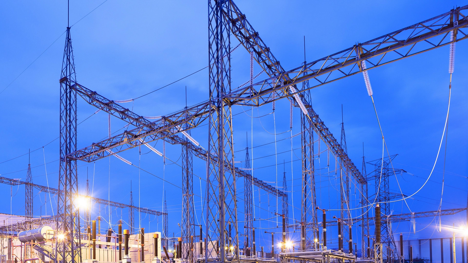 Illuminated electricity substation at dusk.