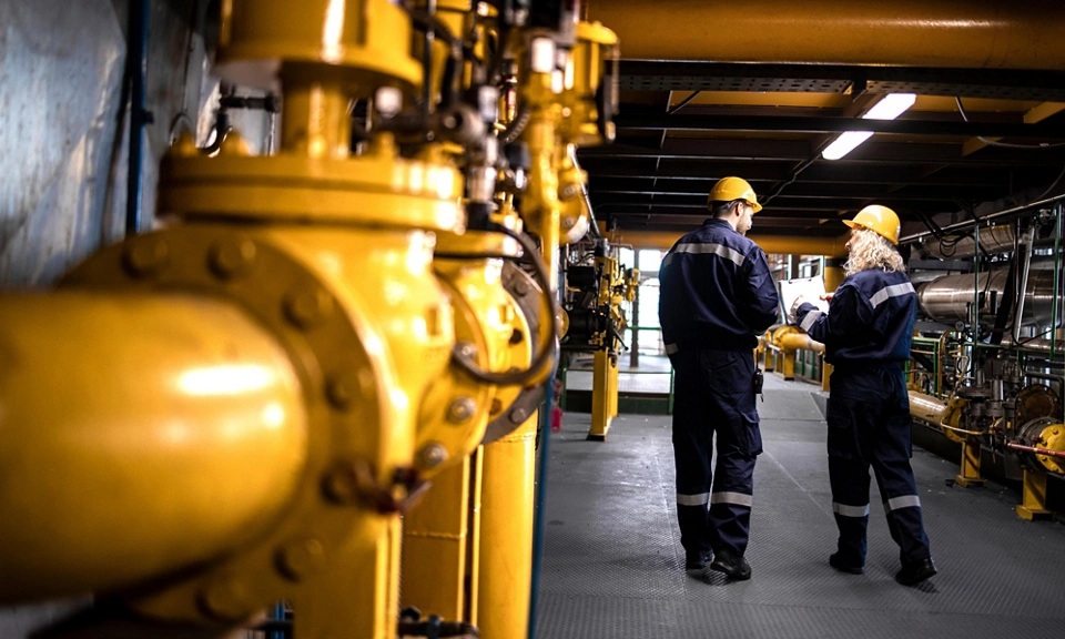 Petrochemical industry, oil and gas production. Factory workers or engineers walking by gas pipelines inside refinery production plant.