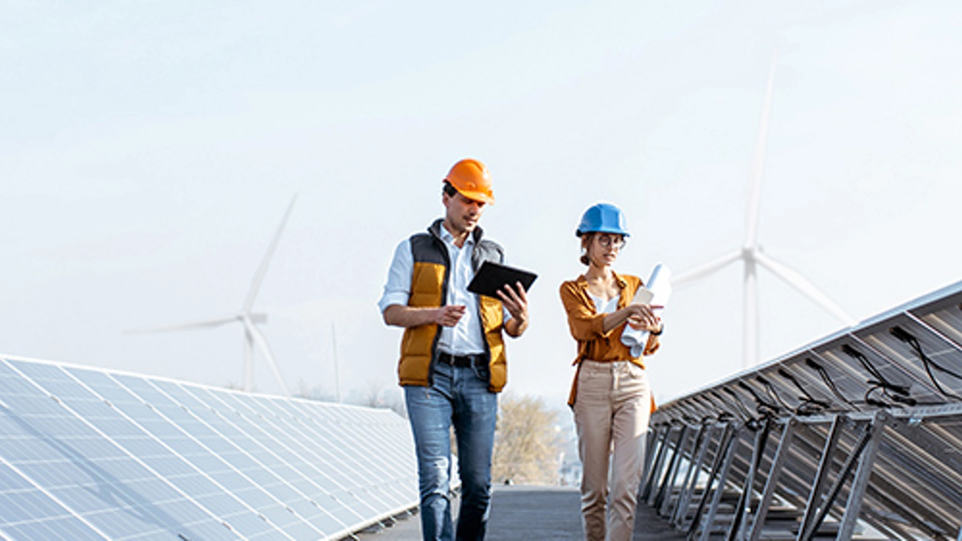 View on the rooftop solar power plant with two engineers walking and examining photovoltaic panels. Concept of alternative energy and its service