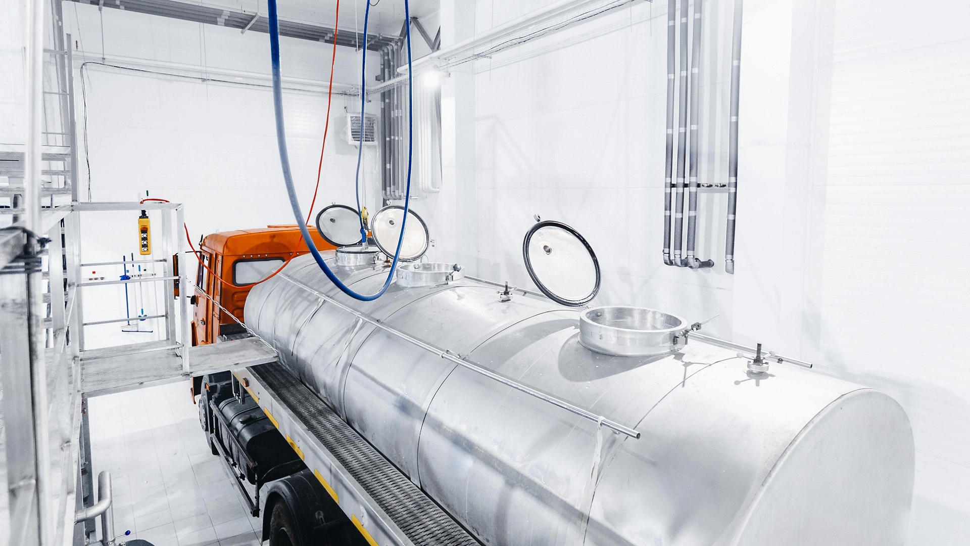 Milk tanker truck pumps products into steel storage tanks, dairy factory industry.